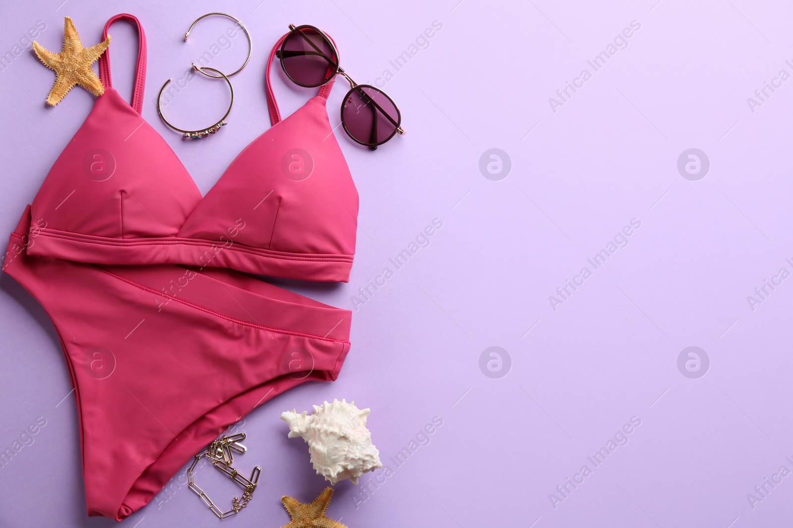 Photo of Beautiful pink bikini and beach accessories on lilac background, flat lay. Space for text