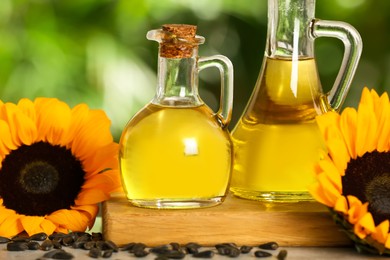 Sunflower cooking oil, seeds and yellow flowers on light grey table outdoors, closeup