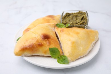 Photo of Delicious samosas with basil and pesto sauce on white marble table, closeup