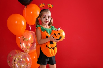 Cute little girl with pumpkin candy bucket and balloons wearing Halloween costume on red background. Space for text