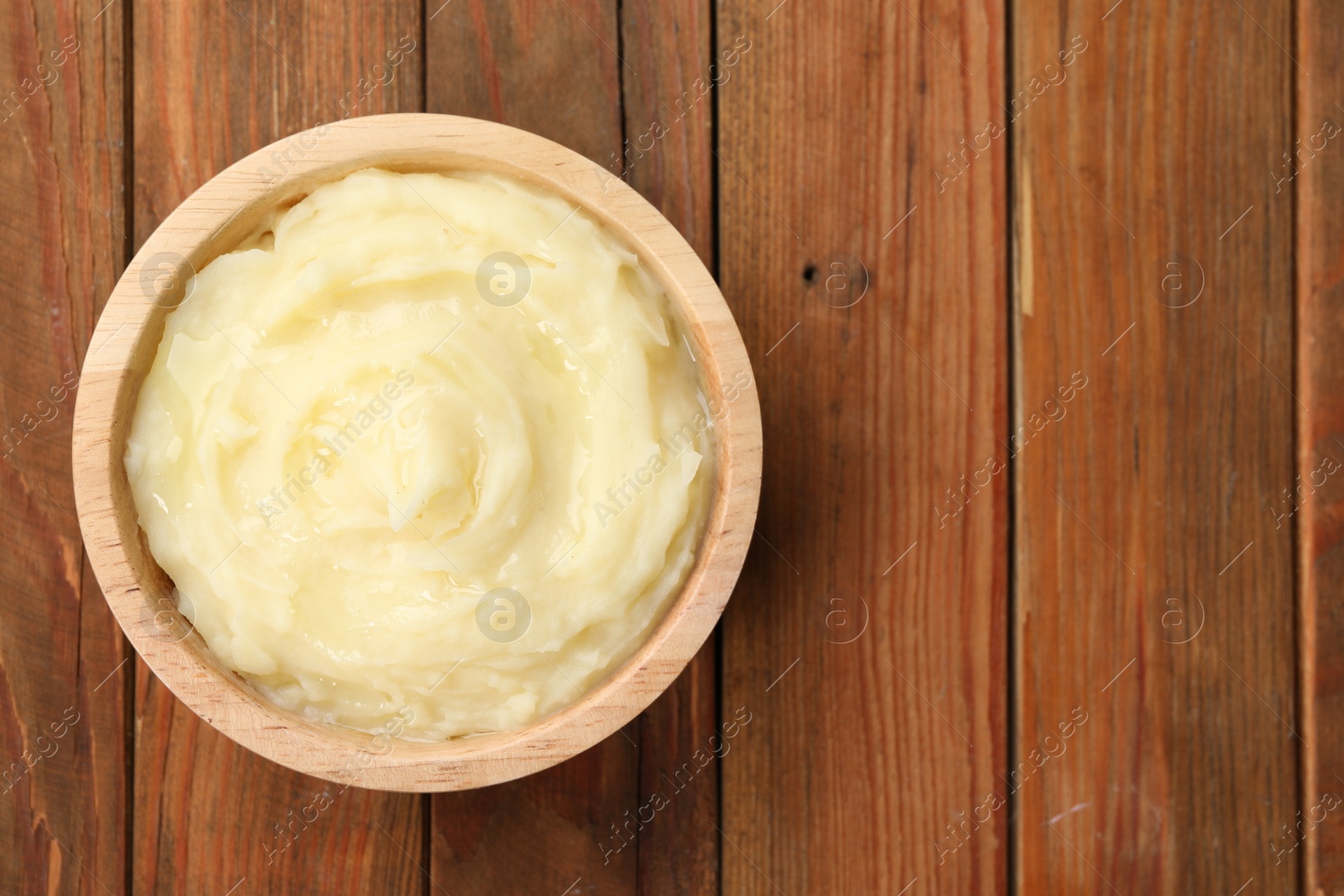 Photo of Bowl of tasty mashed potato on wooden table, top view. Space for text