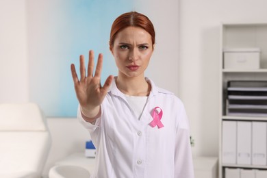 Photo of Mammologist with pink ribbon showing stop gesture in hospital. Breast cancer awareness