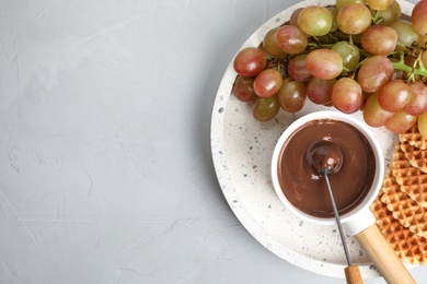 Photo of Fondue pot with chocolate and grape on grey table, top view. Space for text