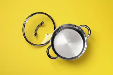 Steel pot and glass lid on yellow background, flat lay