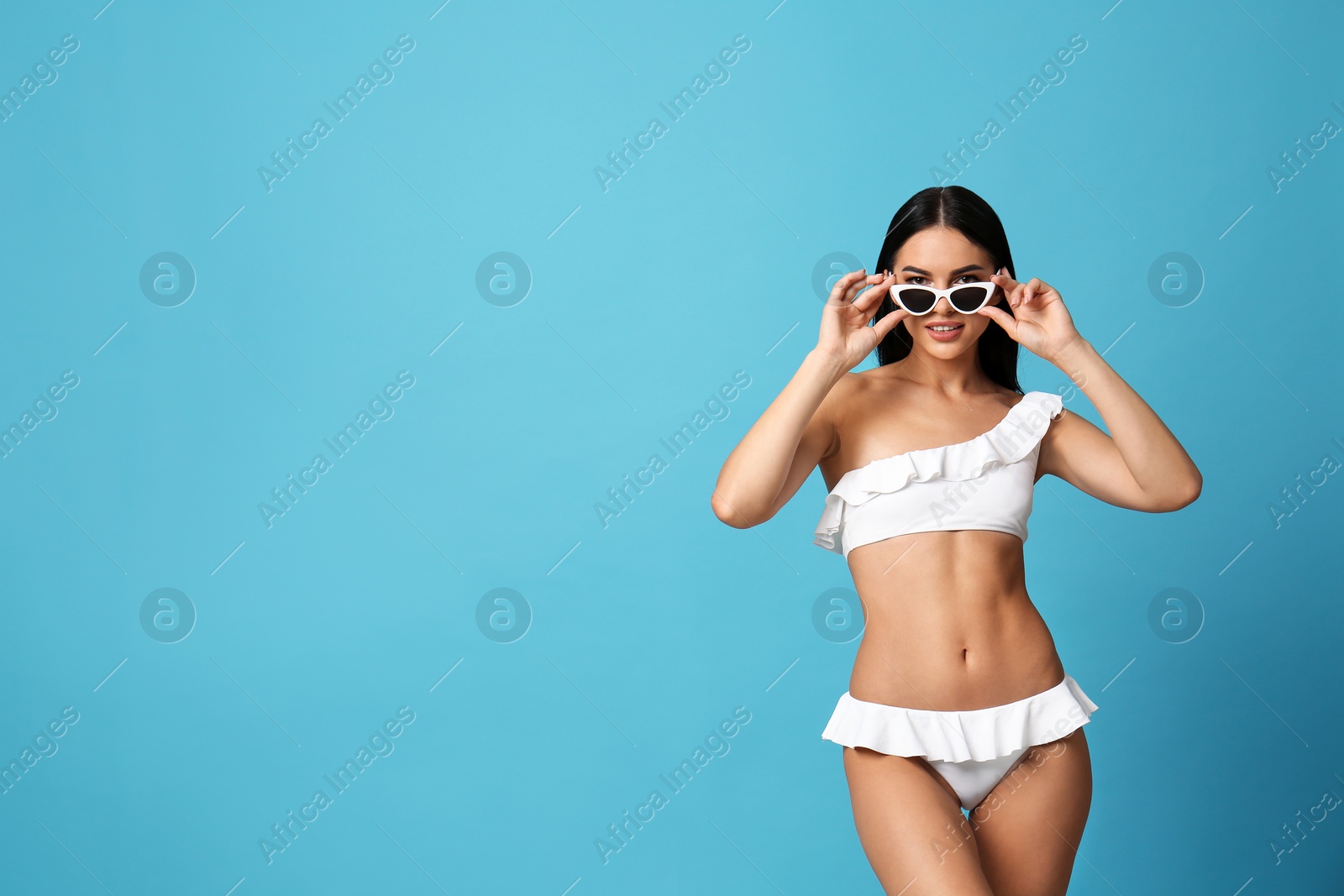 Photo of Beautiful young woman in white bikini with sunglasses on light blue background. Space for text