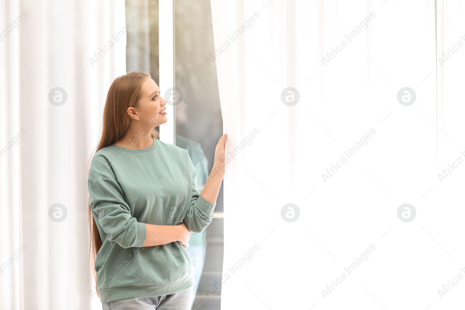 Photo of Beautiful young woman looking out of window at home