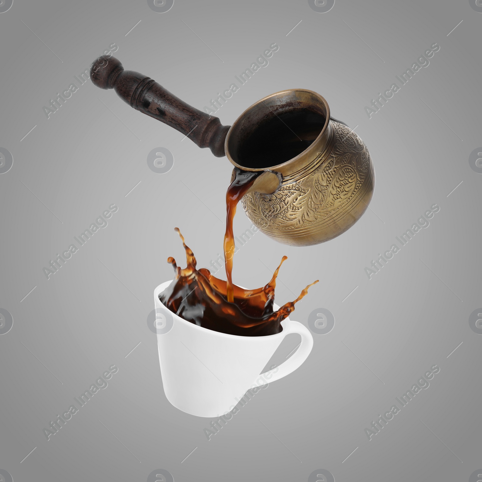 Image of Pouring freshly brewed aromatic coffee from turkish pot into cup. Objects in air on grey background