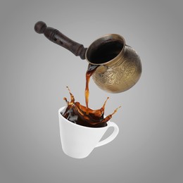 Image of Pouring freshly brewed aromatic coffee from turkish pot into cup. Objects in air on grey background