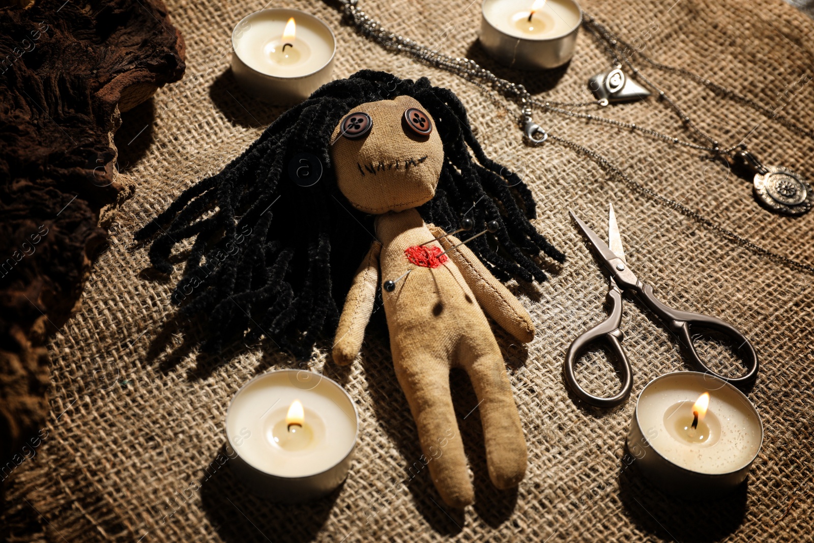 Photo of Voodoo doll with pins surrounded by ceremonial items on burlap fabric