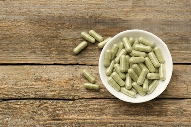 Photo of Vitamin capsules in bowl on wooden table, top view. Space for text
