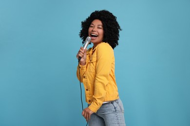 Beautiful woman with microphone singing on light blue background