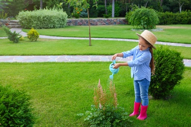 Photo of Little girl watering flowers in backyard. Home gardening