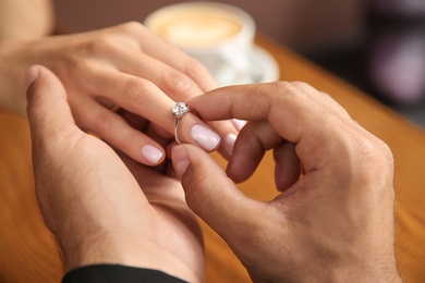 Photo of Man putting engagement ring on his girlfriend's finger in cafe, closeup