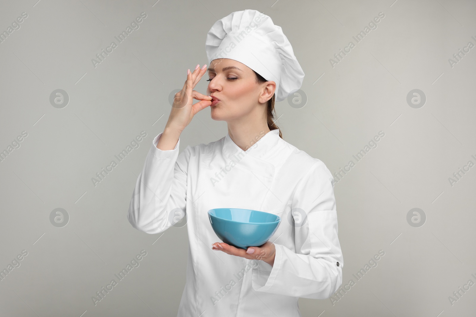 Photo of Woman chef in uniform holding bowl and showing perfect sign on grey background