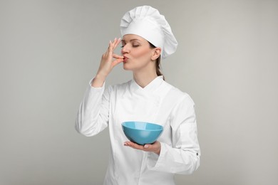 Photo of Woman chef in uniform holding bowl and showing perfect sign on grey background