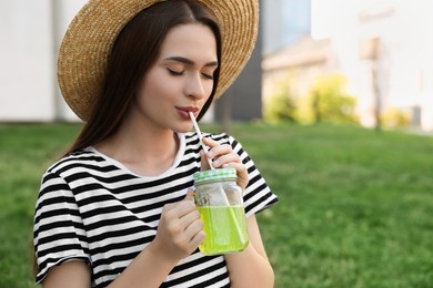 Photo of Young woman in straw hat with mason jar of fresh juice on green grass outdoors, space for text