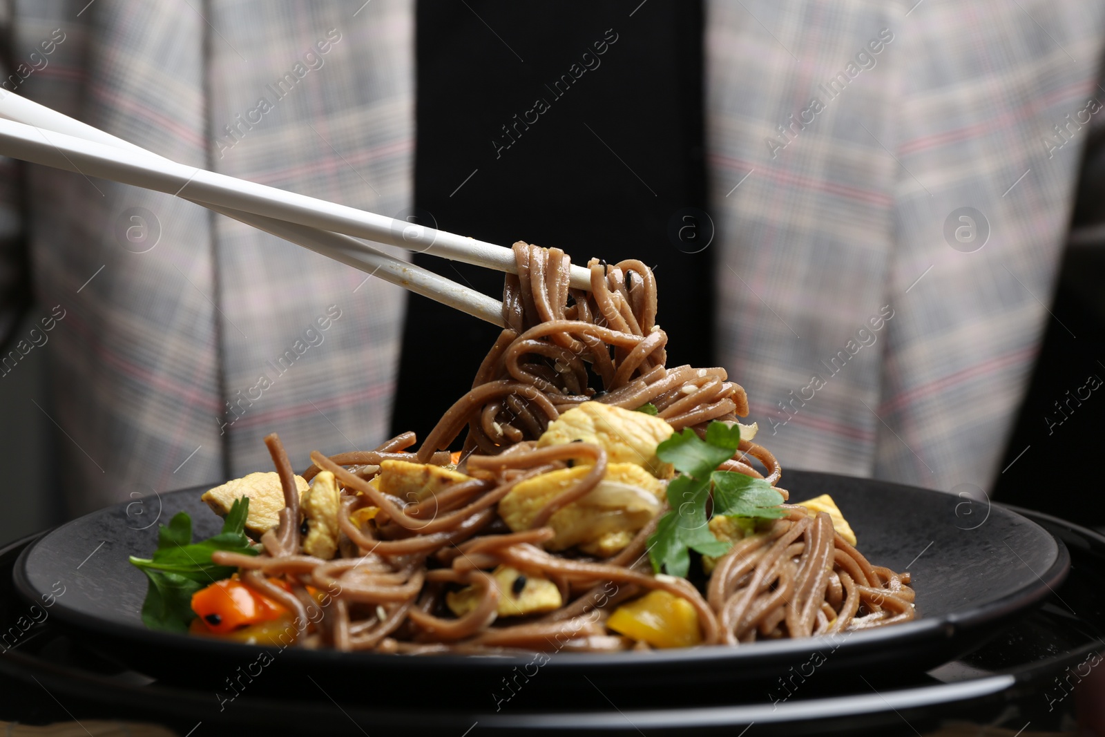 Photo of Stir-fry. Woman eating tasty noodles with meat and vegetables at table, closeup