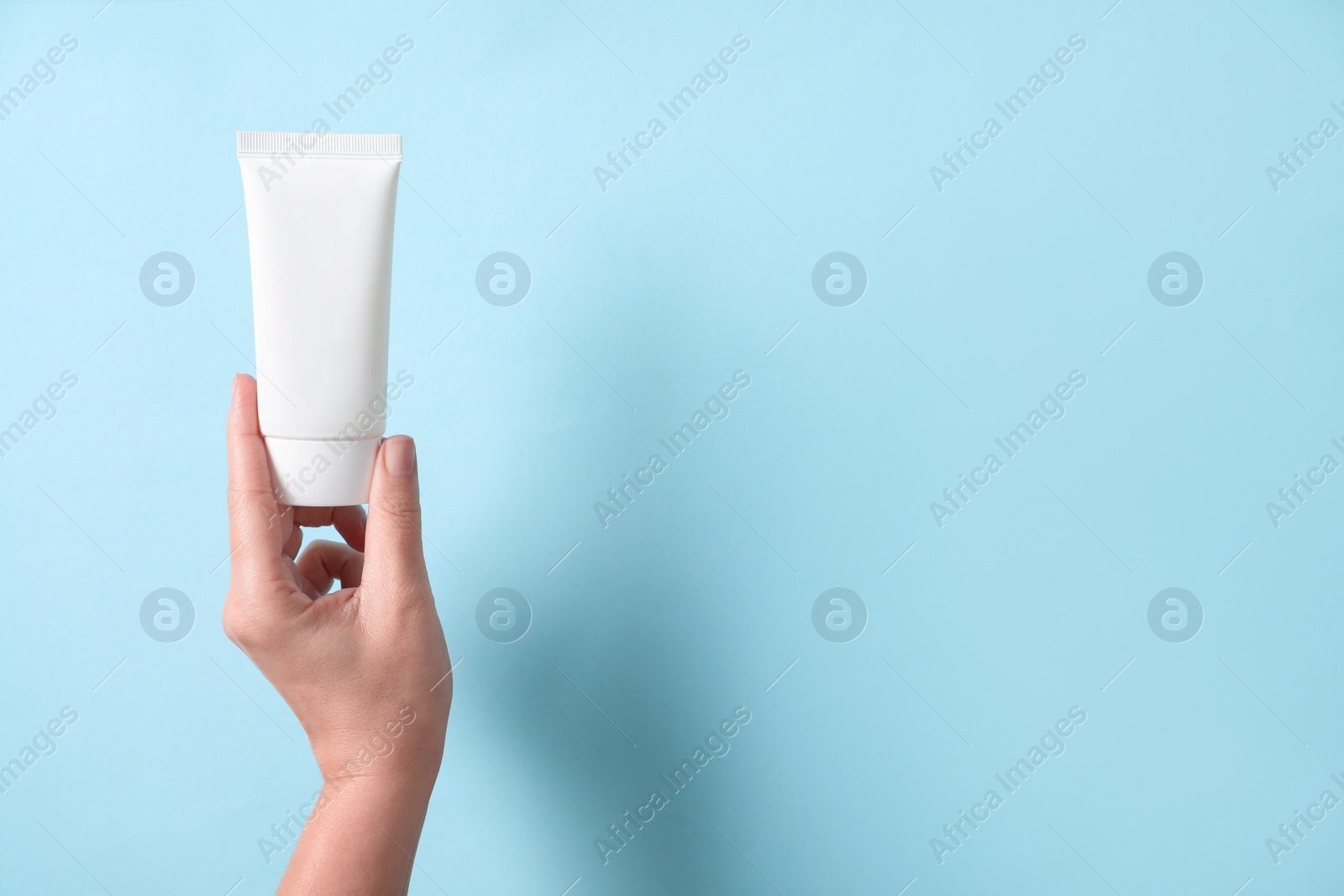 Photo of Woman with tube of hand cream on light blue background, closeup. Space for text