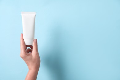 Woman with tube of hand cream on light blue background, closeup. Space for text