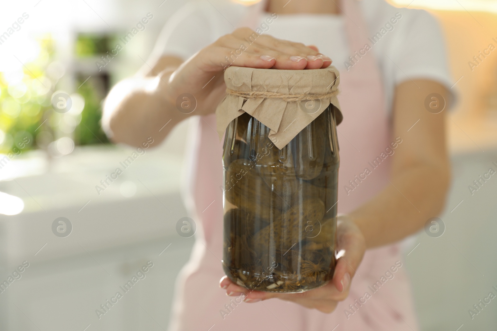 Photo of Woman holding jar of pickled cucumbers indoors, closeup