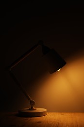 Photo of Stylish modern desk lamp on wooden table at night