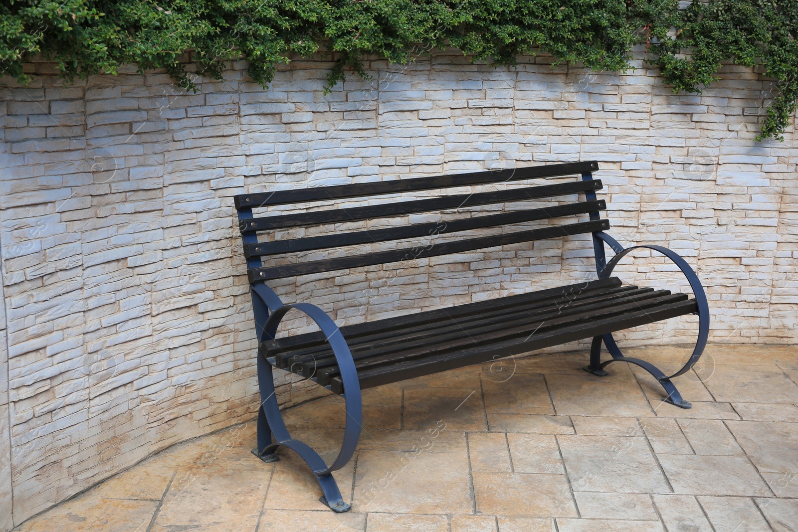 Photo of Beautiful wooden bench near brick wall on pavement outdoors