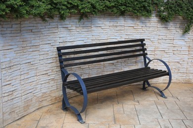 Beautiful wooden bench near brick wall on pavement outdoors