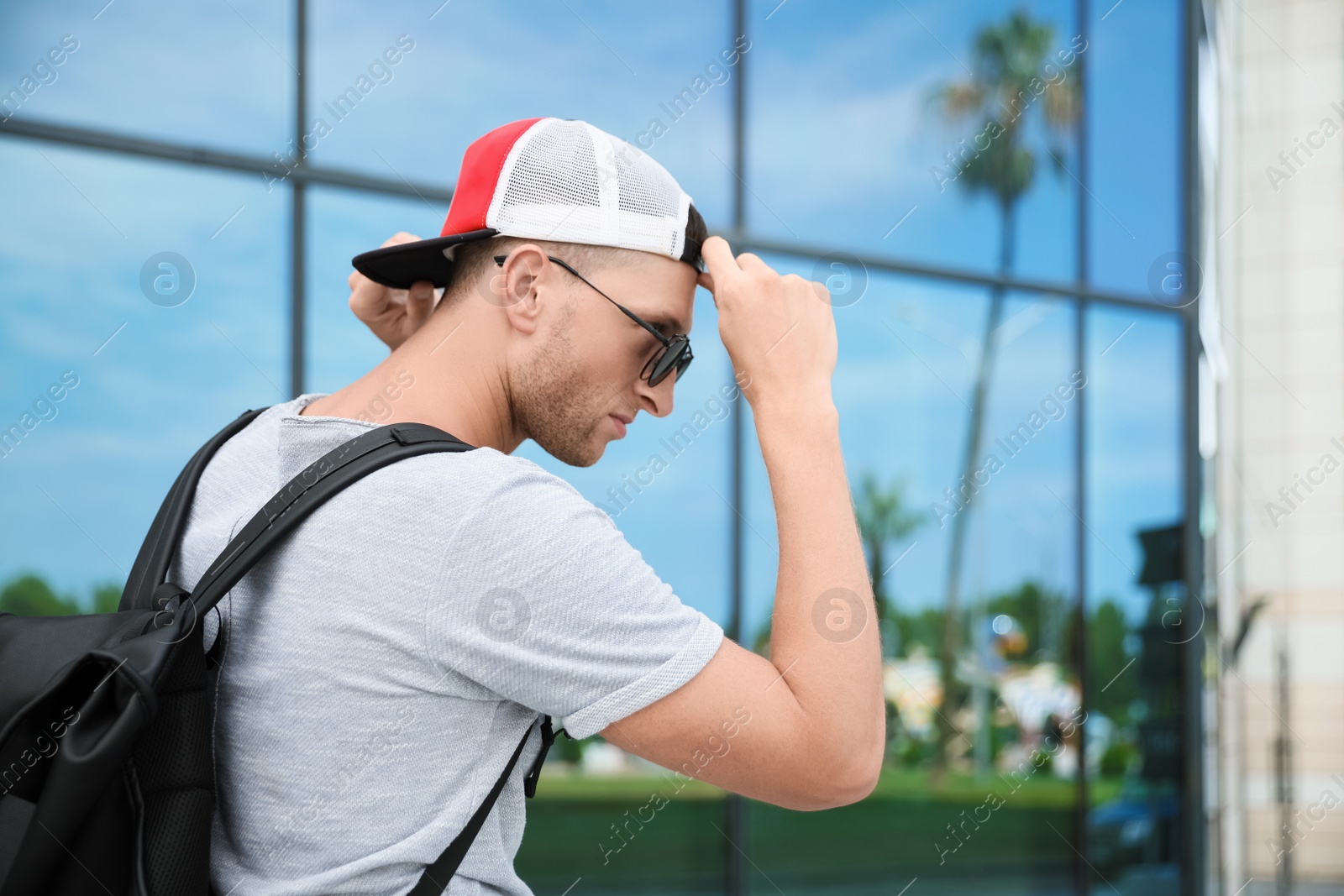 Photo of Handsome young man with stylish sunglasses and backpack near building outdoors, space for text