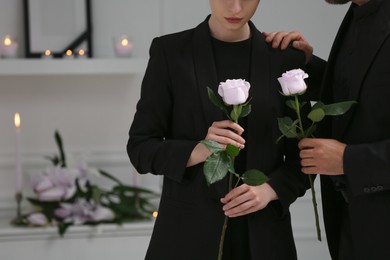 Image of Couple with violet roses mourning indoors, closeup and space for text. Funeral ceremony