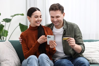 Happy couple with smartphone and credit card shopping online together at home
