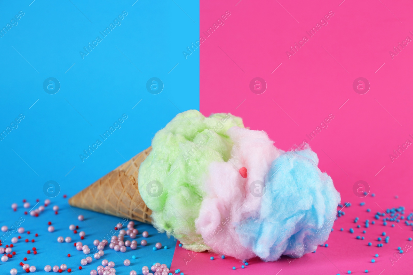 Photo of Sweet cotton candy in waffle cone on color background, closeup