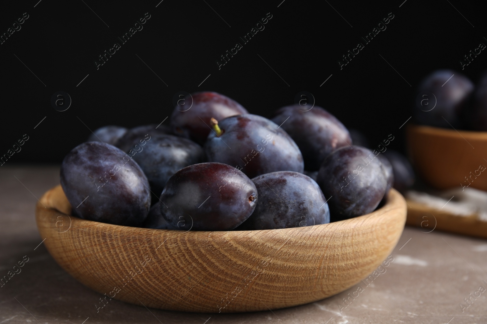 Photo of Delicious ripe plums in wooden bowl on grey marble table, closeup