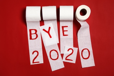 Photo of Toilet paper with text Bye 2020 on red background, flat lay
