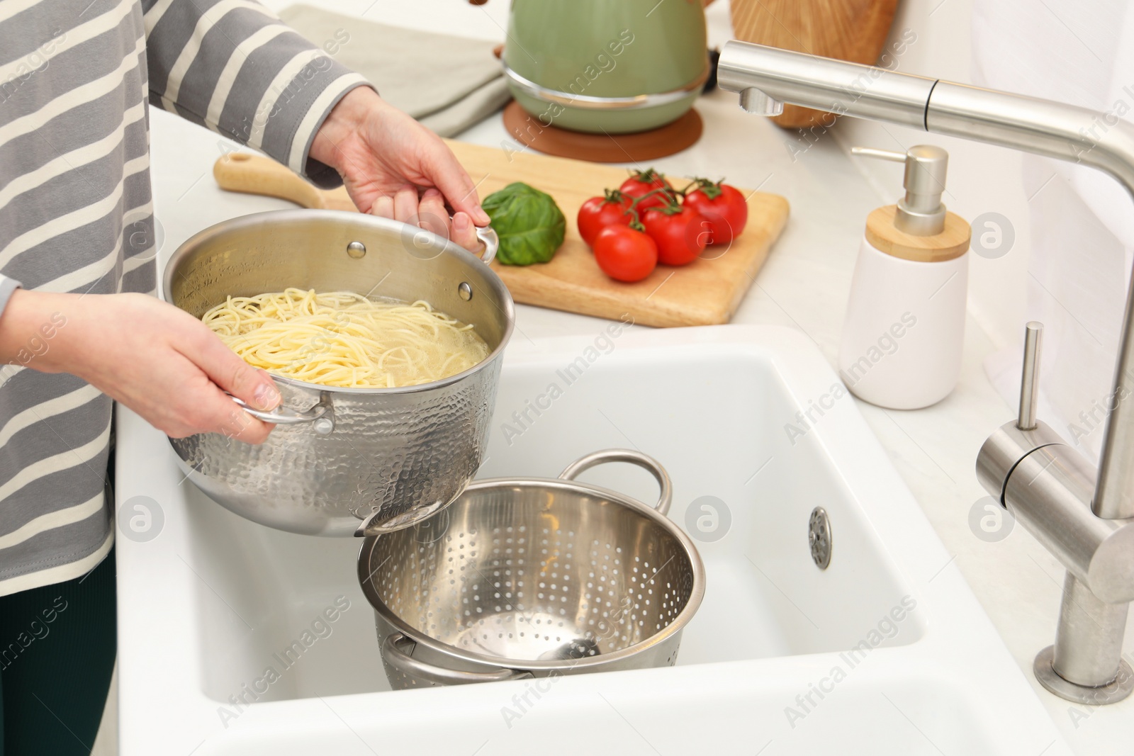 Photo of Woman draining pasta into colander at sink, closeup