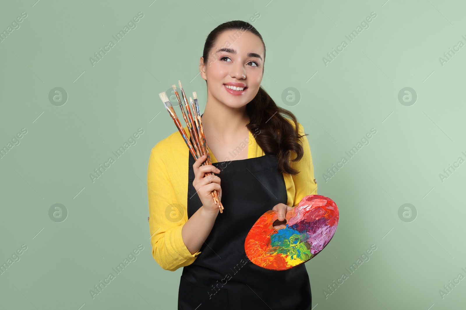 Photo of Woman with painting tools on pale green background. Young artist