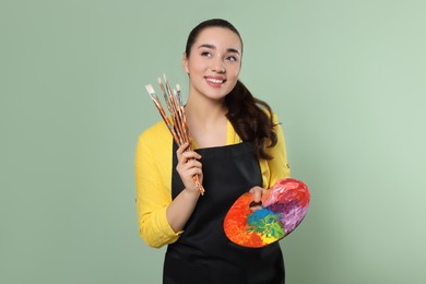Photo of Woman with painting tools on pale green background. Young artist
