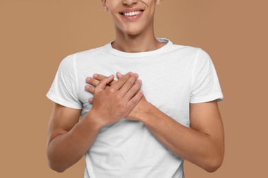 Photo of Thank you gesture. Grateful man with hands on chest against brown background, closeup