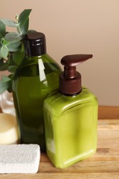 Bottles of shampoo on wooden table near beige wall, closeup