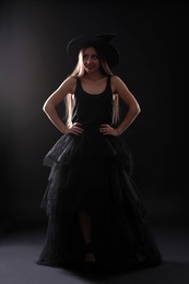 Photo of Young woman wearing witch costume on black background. Halloween party