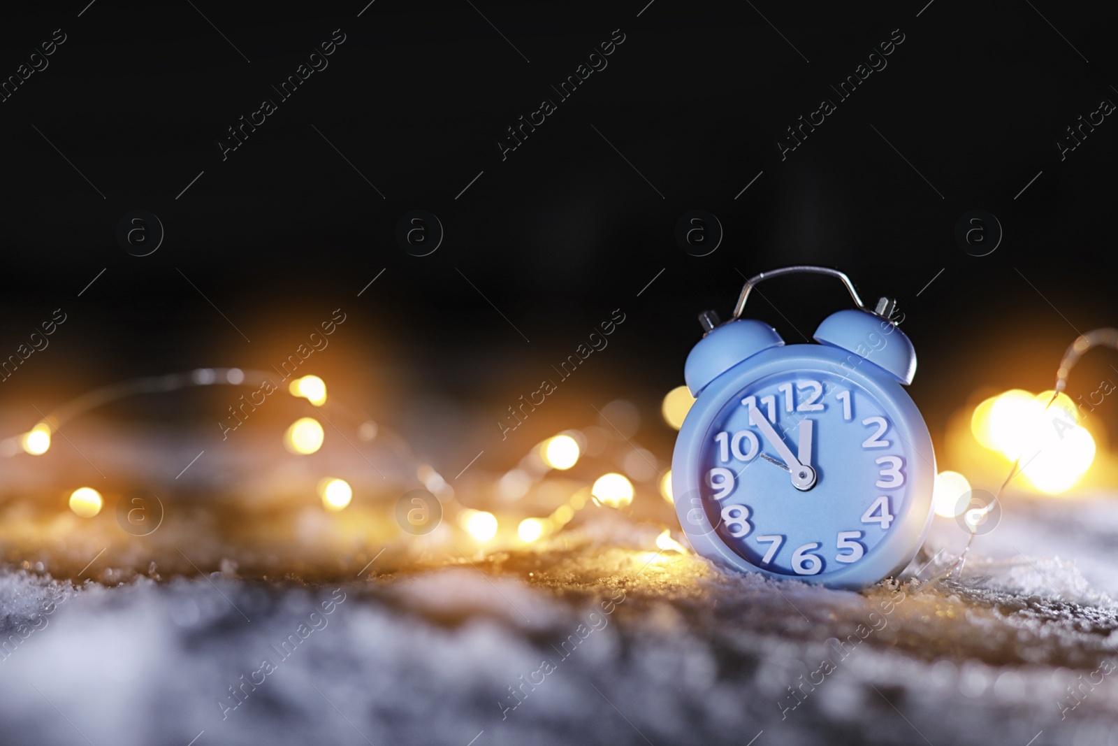 Photo of Alarm clock and Christmas lights on white snow outdoors, space for text. Midnight countdown