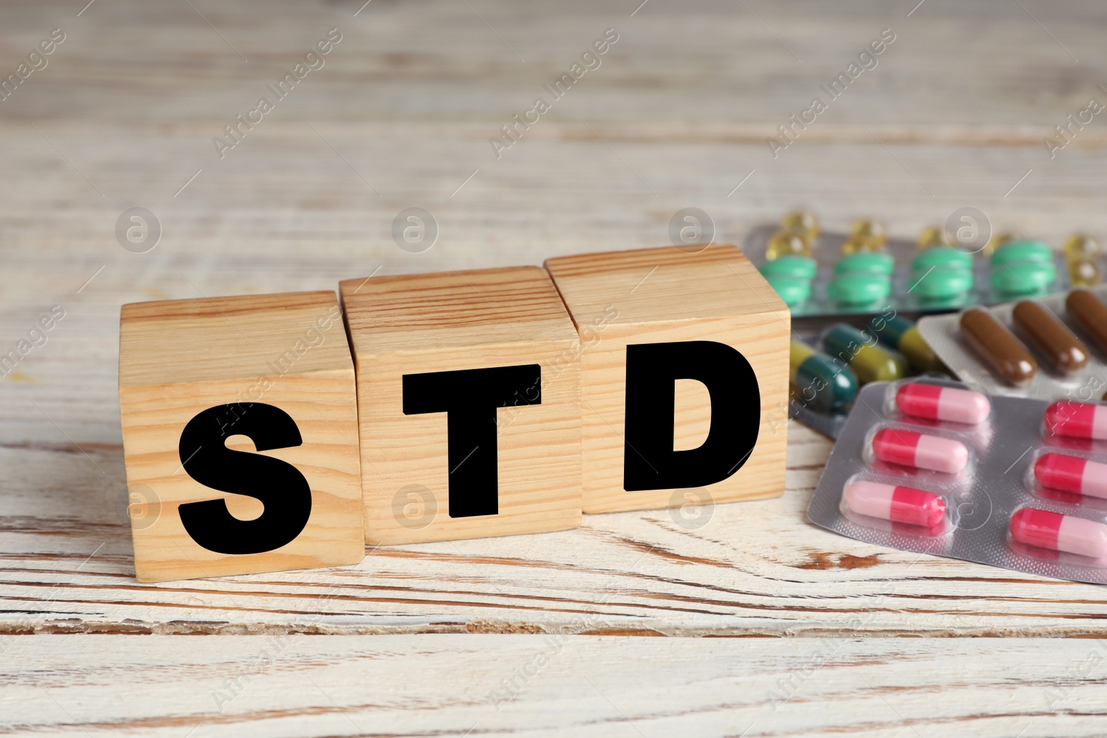 Photo of Abbreviation STD made with cubes near pills on white wooden table