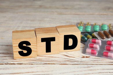 Photo of Abbreviation STD made with cubes near pills on white wooden table