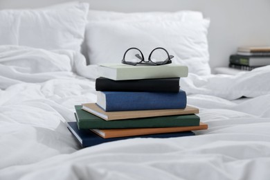 Photo of Hardcover books and glasses on bed indoors