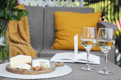 Vase with roses, open book, glasses of wine and snacks on rattan table at balcony