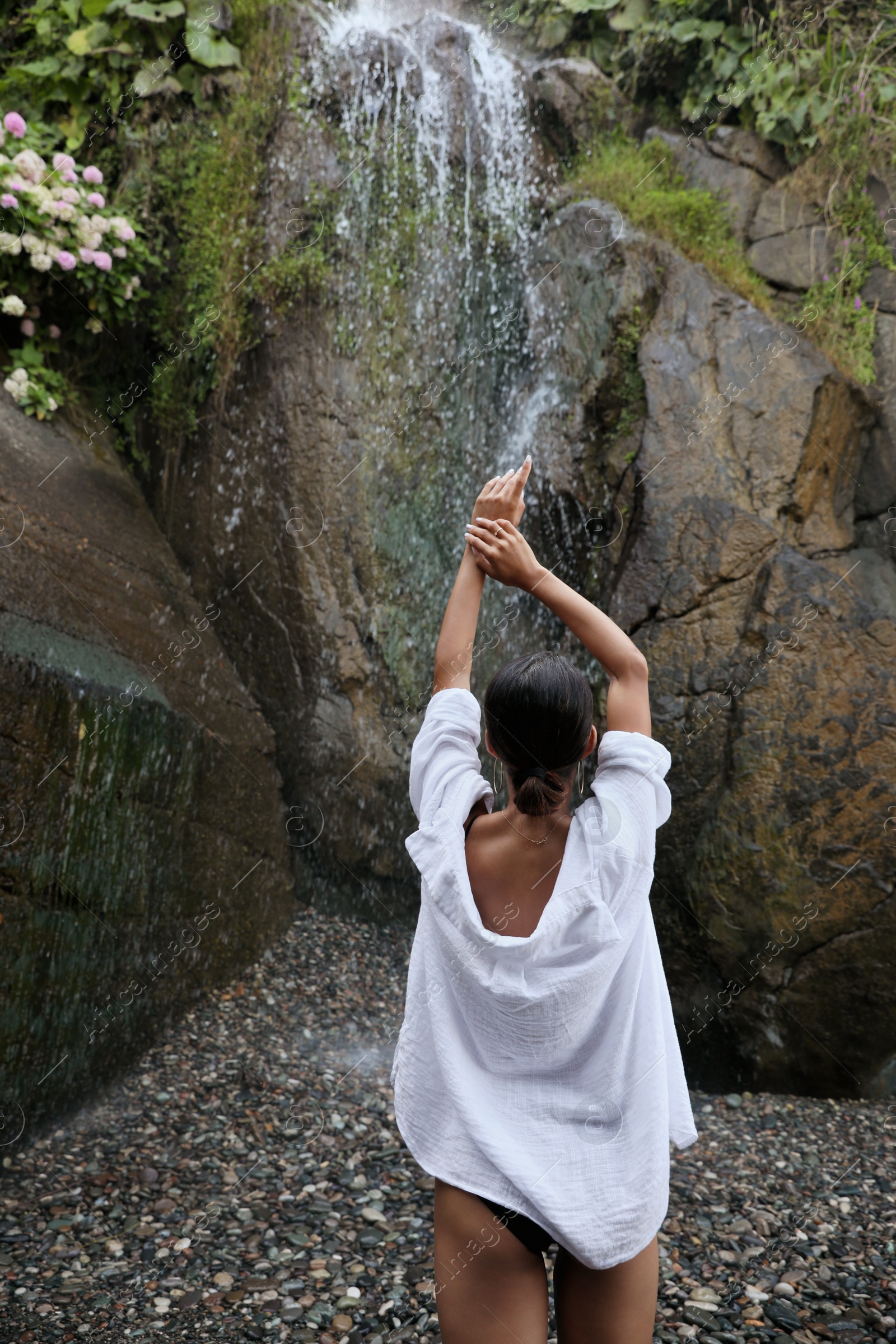 Photo of Young woman near beautiful waterfall outdoors, back view