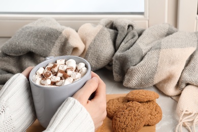 Photo of Woman with cup of cocoa and cookies at window, closeup. Winter drink