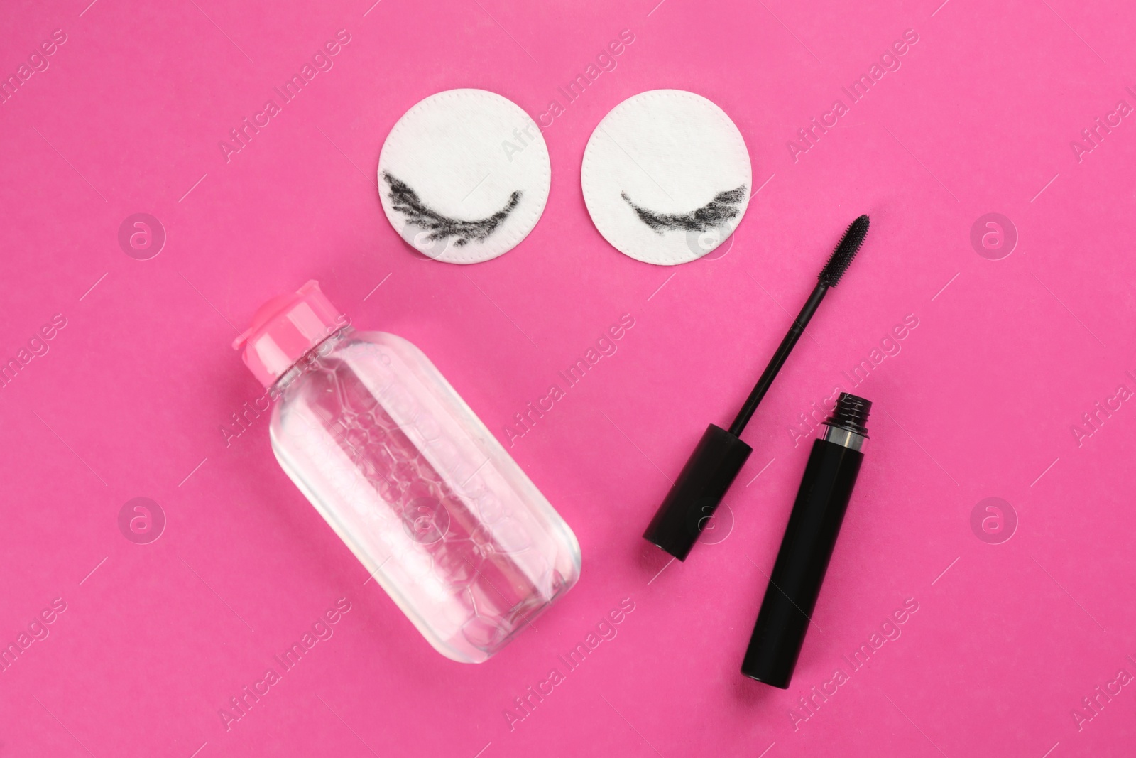 Photo of Dirty cotton pads, mascara and micellar cleansing water on pink background, flat lay