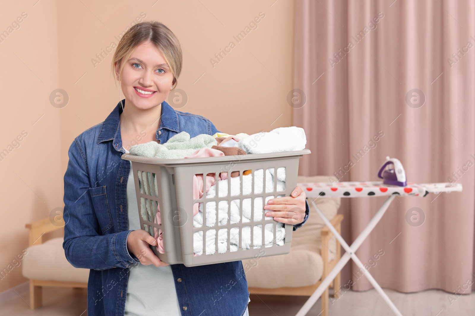 Photo of Happy woman with basket full of laundry at home