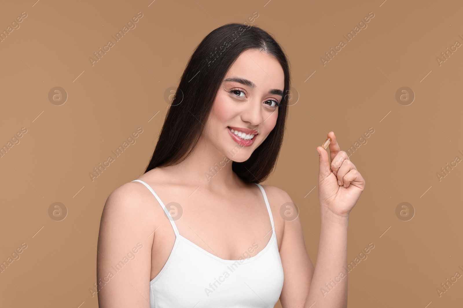 Photo of Beautiful young woman with vitamin pill on beige background