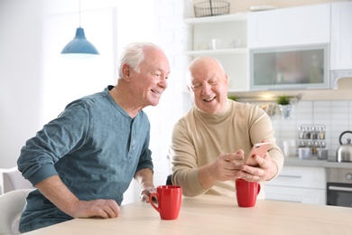 Elderly men using smartphone at table in kitchen